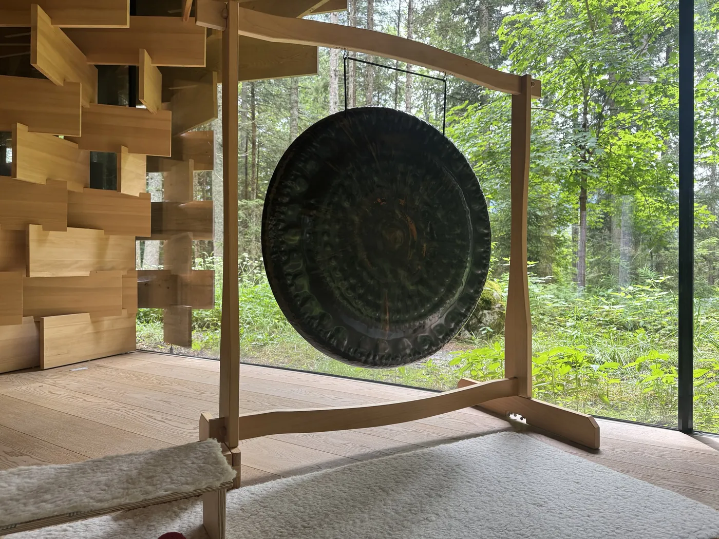 Dunkler Gong auf einem Holzständer vor der Glasfront zum Wald