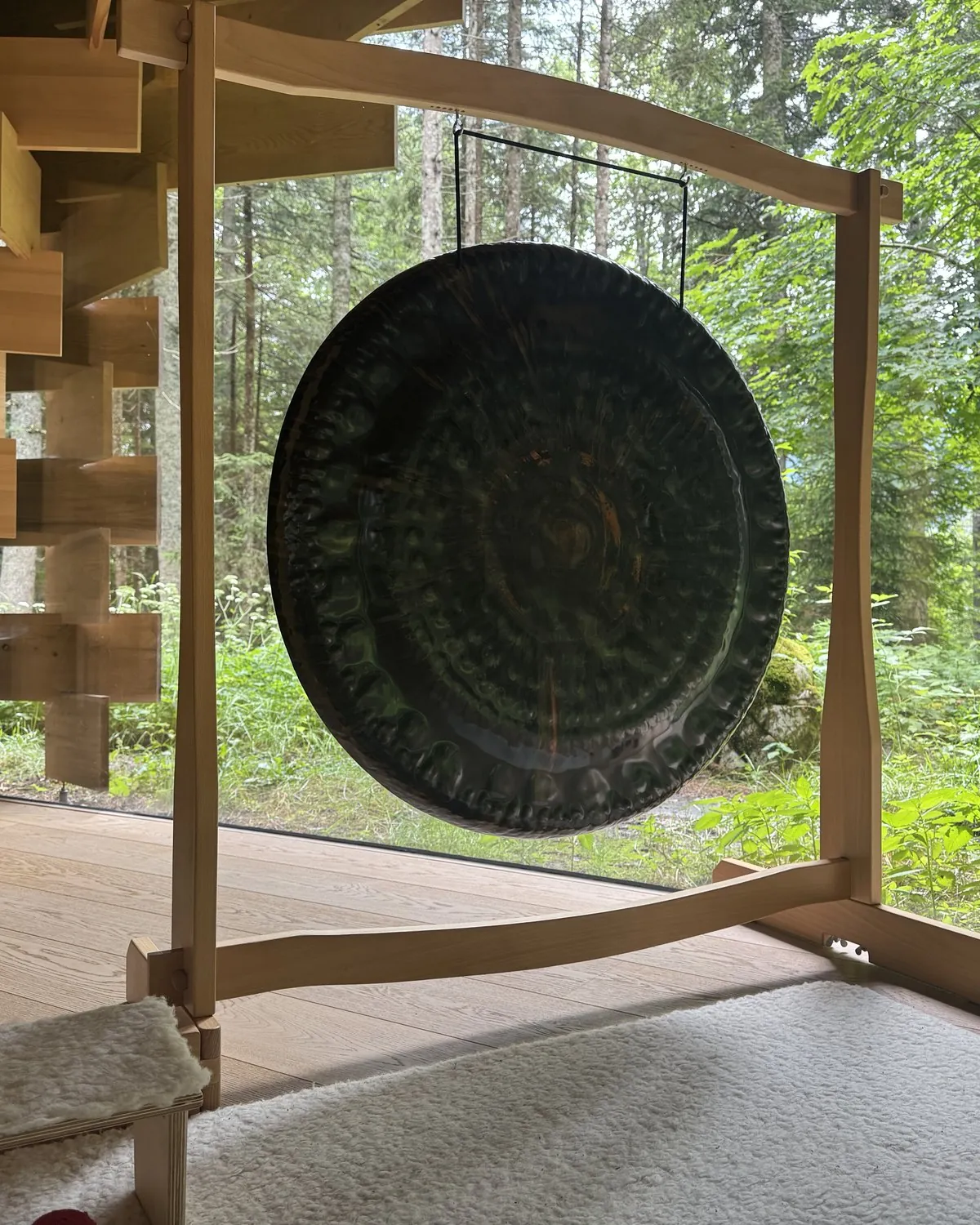 Ein großer Gong im Holzrahmen vor der Waldkulisse hinter Glas