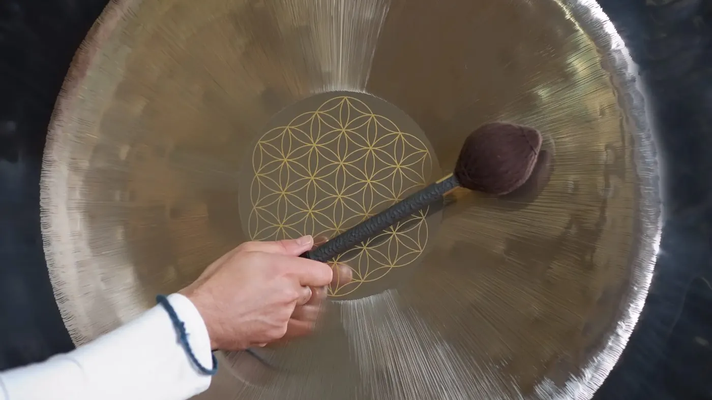 Eine Hand führt das Mallet über die Oberfläche eines Gongs mit goldener Gravur