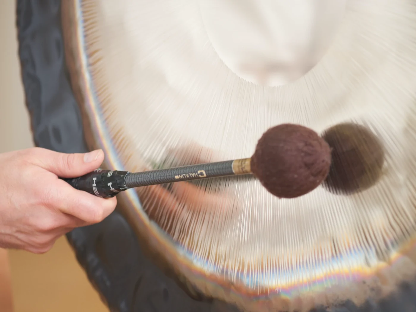 Hand mit Filzschlägel am Gong, der Anschlag ist in Bewegung zu sehen