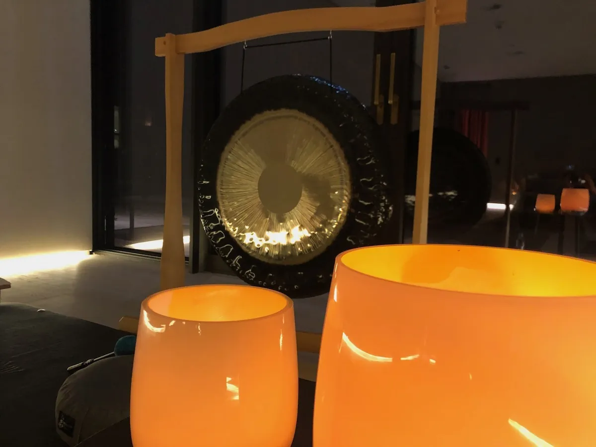 Gong im hellen Holzständer in warmer Abendstimmung, davor zwei leuchtende Klangschalen