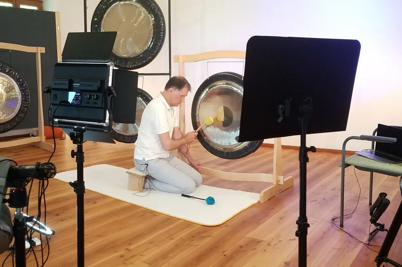 Alexander Renner spielt den Gong im Aufnahmestudio des Online-Kurses, umgeben von Kameras, Licht und Laptop