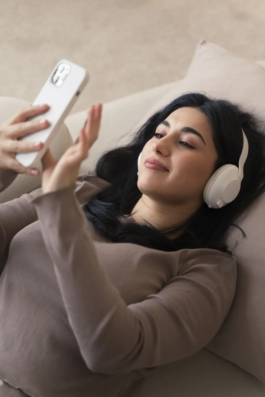Person mit Kopfhörern startet auf einem sandfarbenen Sofa eine Audio-Session auf dem Telefon