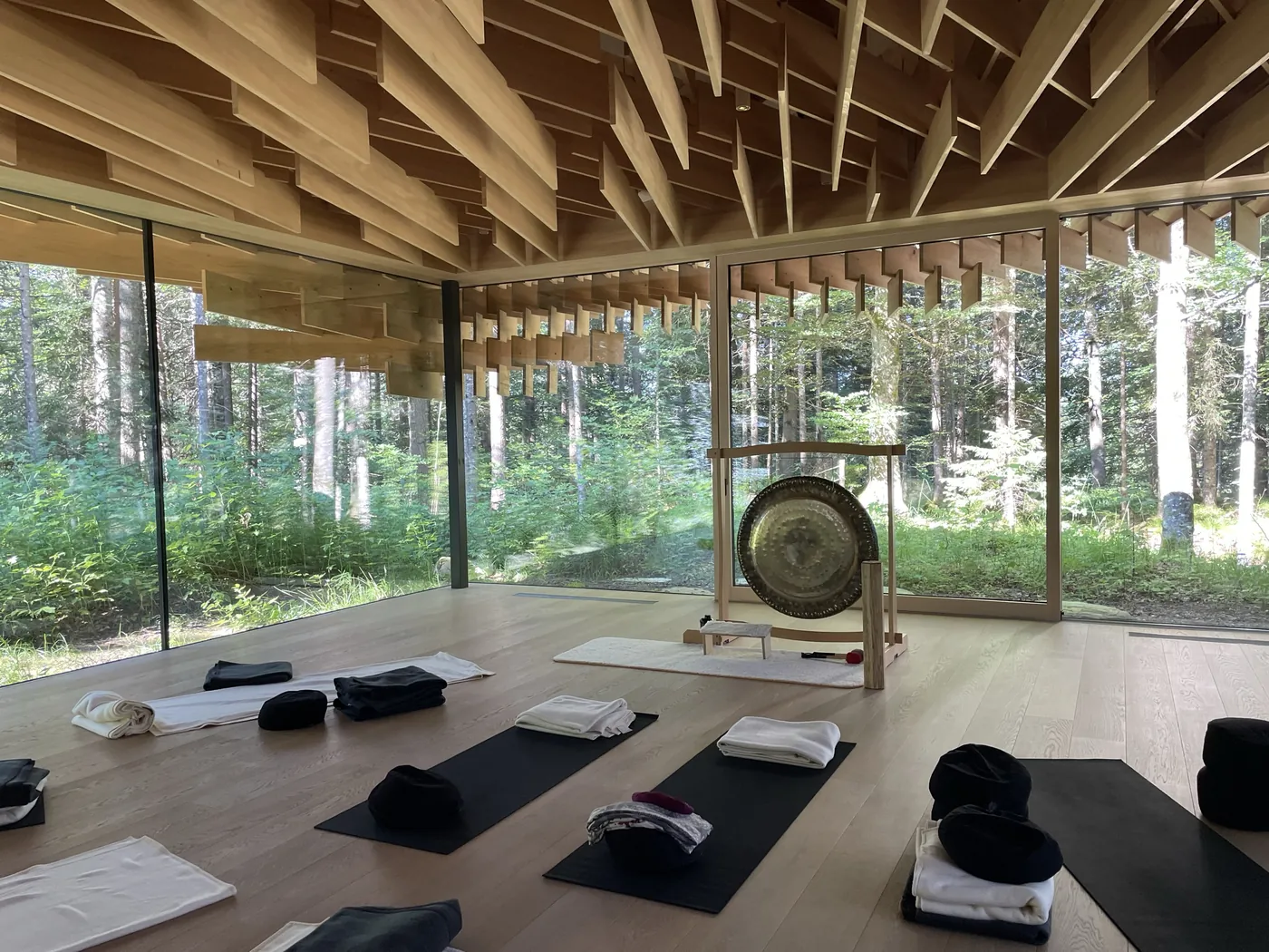 Retreatraum aus Holz und Glas mit einem Gong in der Mitte und Blick in den Wald