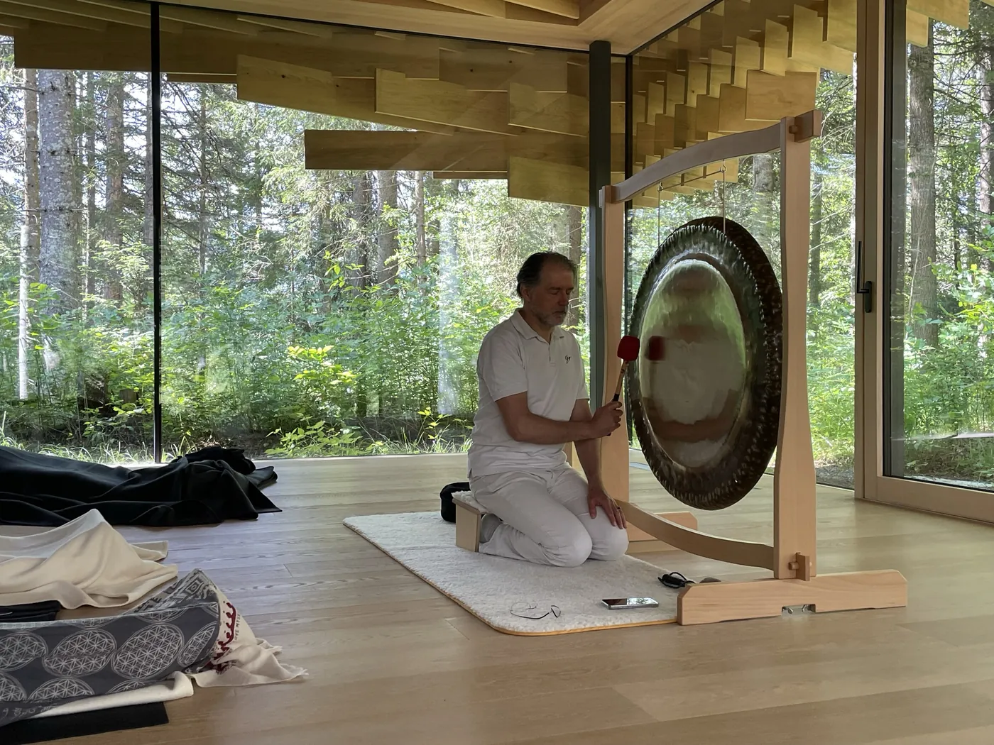 Alexander Renner kniet am Gong in einem Holzraum mit Blick in den Wald