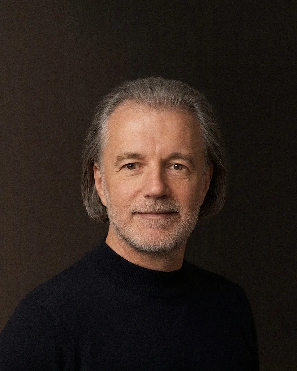 Portrait von Alexander Renner im dunklen Rollkragen vor warmem Studiohintergrund