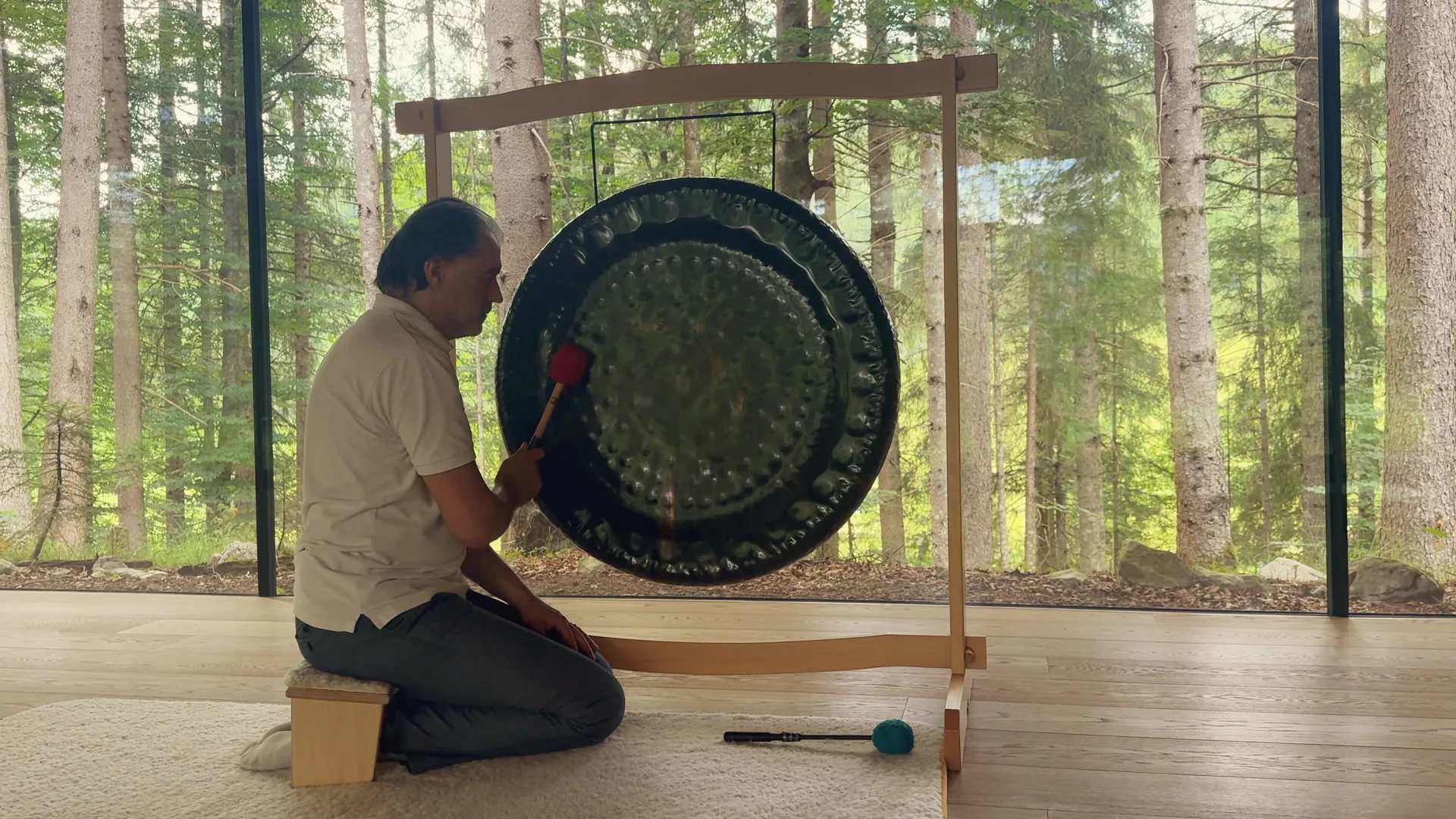Alexander Renner spielt den Gong in einem Meditationsraum aus Glas und Holz mitten im Wald